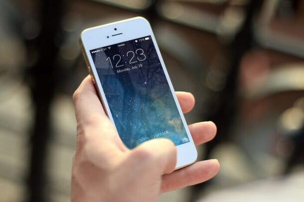 ロック画面が表示されたスマートフォン（iPhone）を手に持つ様子