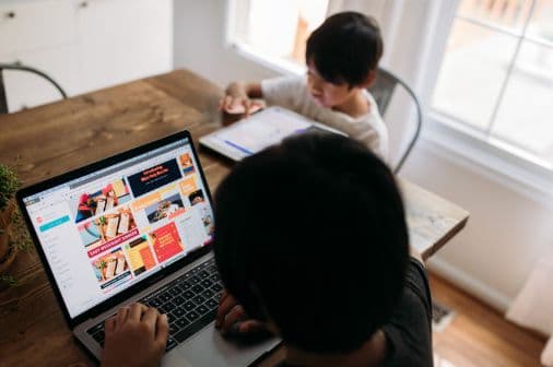 木目のテーブルでパソコンとタブレットを操作する人物